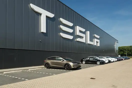 Tesla factory with huge Tesla logo in the wall and few cars parked in fron of it